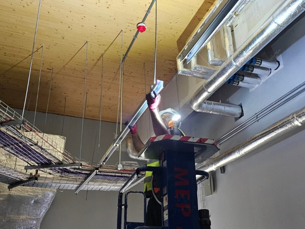 Electrician from Handy Electric Pro installing a commercial LED lighting fixture using a mobile elevated work platform during an electrical installation in Hounslow.